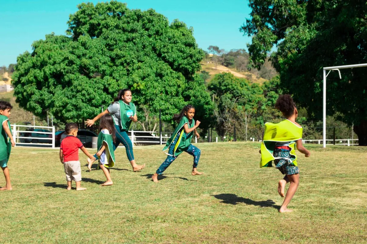 Crianças e monitores brincando em atividade recreativa ao ar livre no Sítio Green Valley, com morros ao fundo