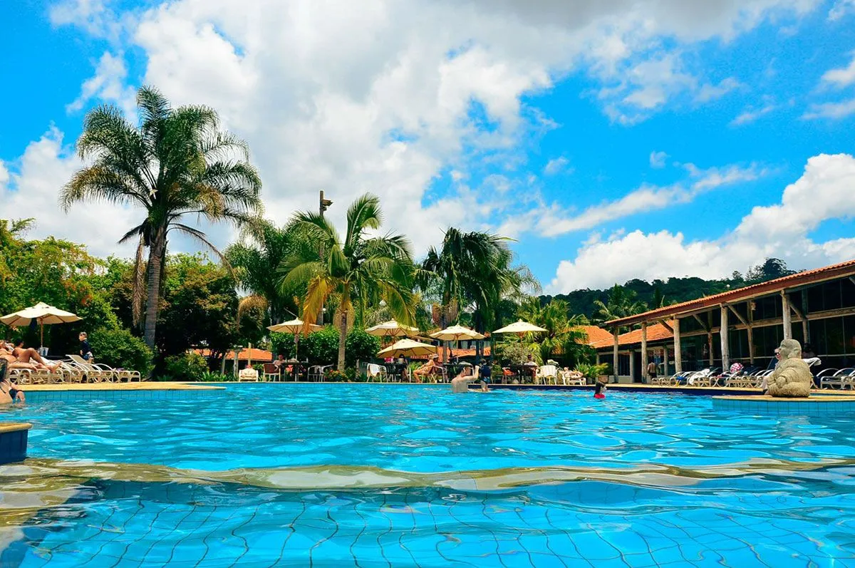 Piscina principal do Hotel Fazenda Hípica Atibaia com hóspedes, palmeiras e o restaurante ao fundo