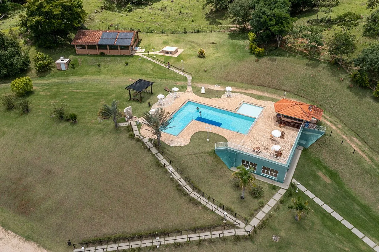 Vista aérea da piscina, deque e prédio central do Bougainville Hotel Fazenda cercado de gramado