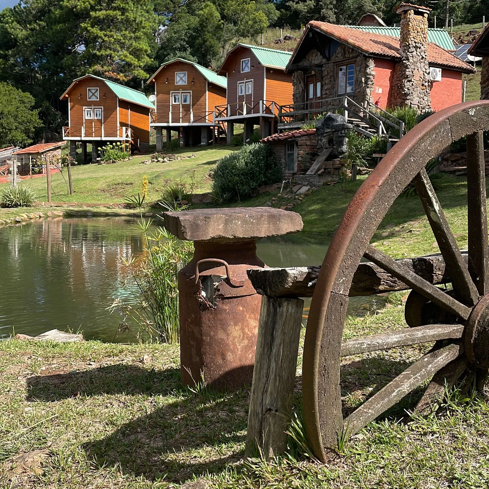 Chalés coloridos à beira de um lago no Fazenda Hotel Invernadinha, com roda de carroça em primeiro plano