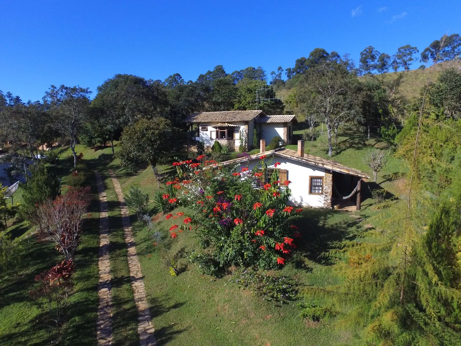 Vista aérea de dois chalés dos Chalés de Minas cercados por vegetação e flores vermelhas