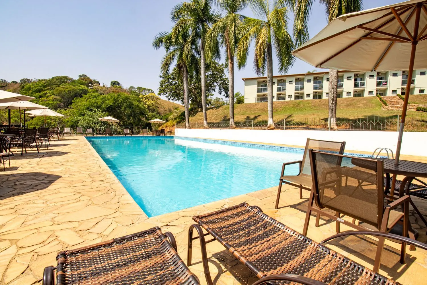 Piscina ao ar livre do Hotel Fazenda Vale da Cachoeira com palmeiras e espreguiçadeiras