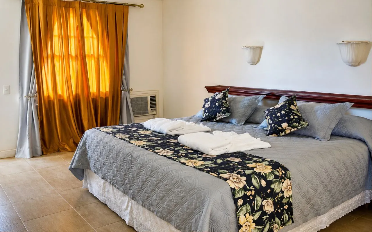 Quarto do Hotel Fazenda Florença com cama de casal, cortina laranja e toalhas dobradas