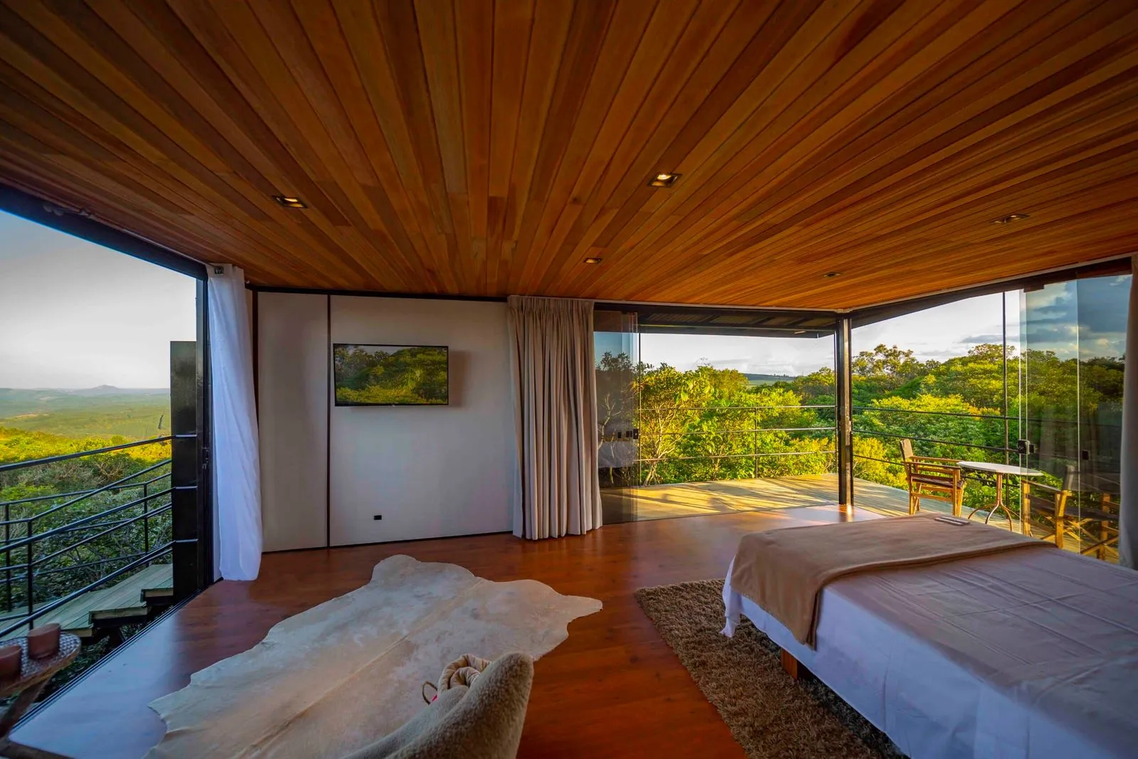 Quarto de chalé do Hotel Fazenda Cainã com parede de vidro e vista para a paisagem ao entardecer