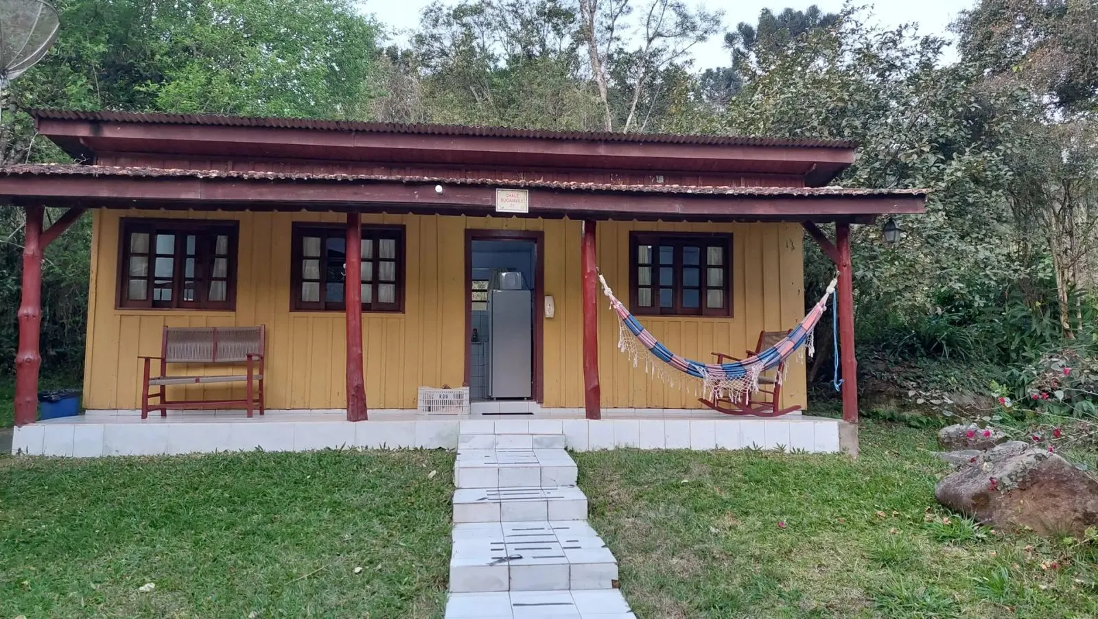 Fachada de chalé amarelo com varanda, rede e bancos na Pousada Fazenda Ribeirão das Flores