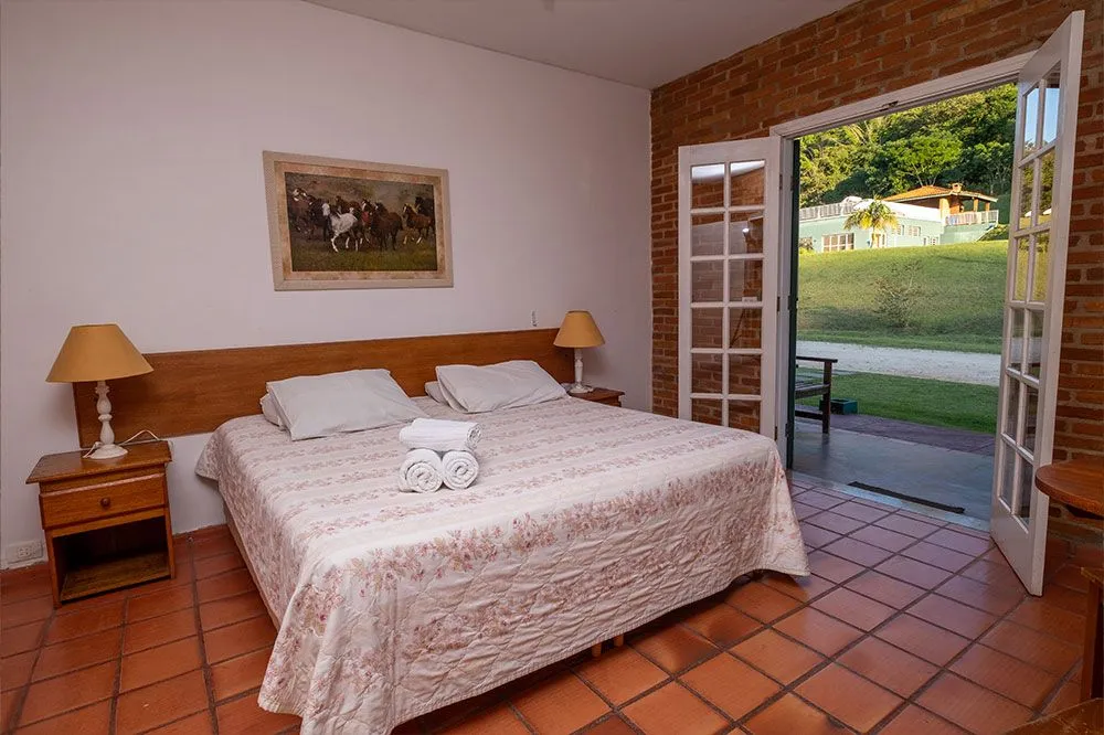 Quarto de casal com piso de cerâmica e porta de vidro aberta para o jardim