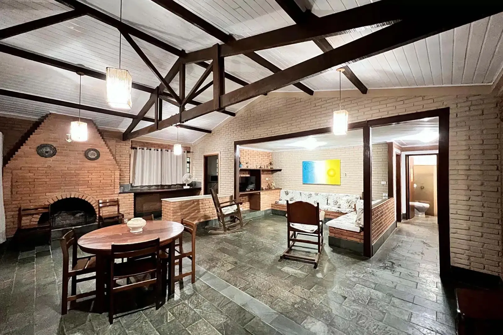 Sala de estar de chalé com lareira de tijolos, mesa de madeira e cadeiras de balanço