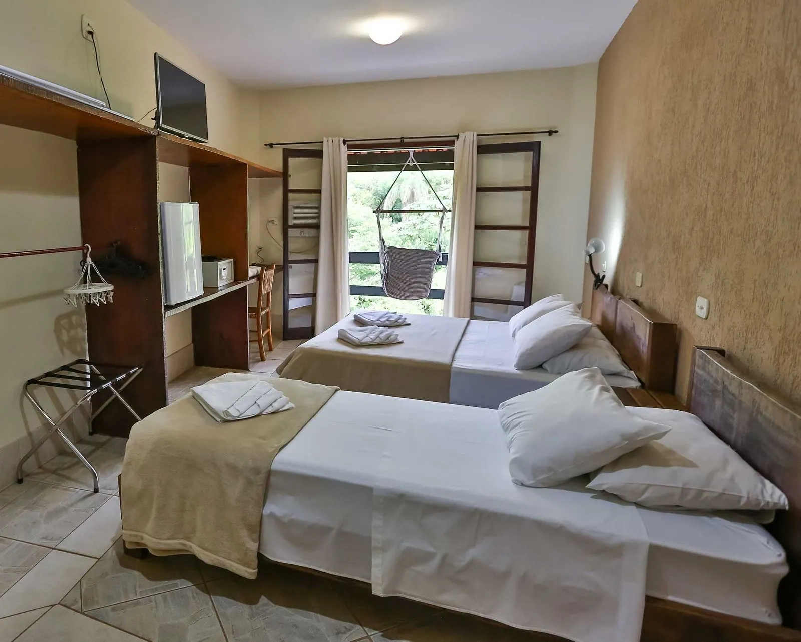 Quarto com duas camas, rede de balanço na janela e vista para o verde