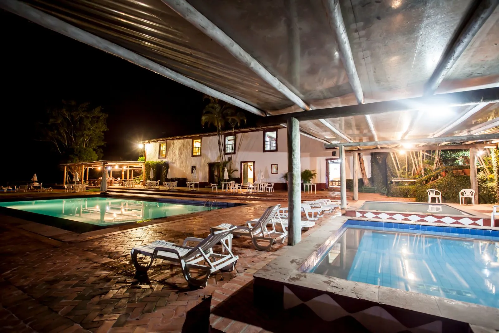 Piscinas iluminadas à noite, com hidromassagem em primeiro plano e o casarão ao fundo