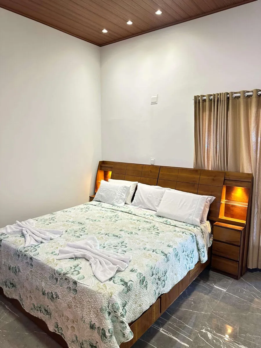 Quarto do Sítio Green Valley com cama de casal, cabeceira de madeira com luz embutida e toalhas dobradas