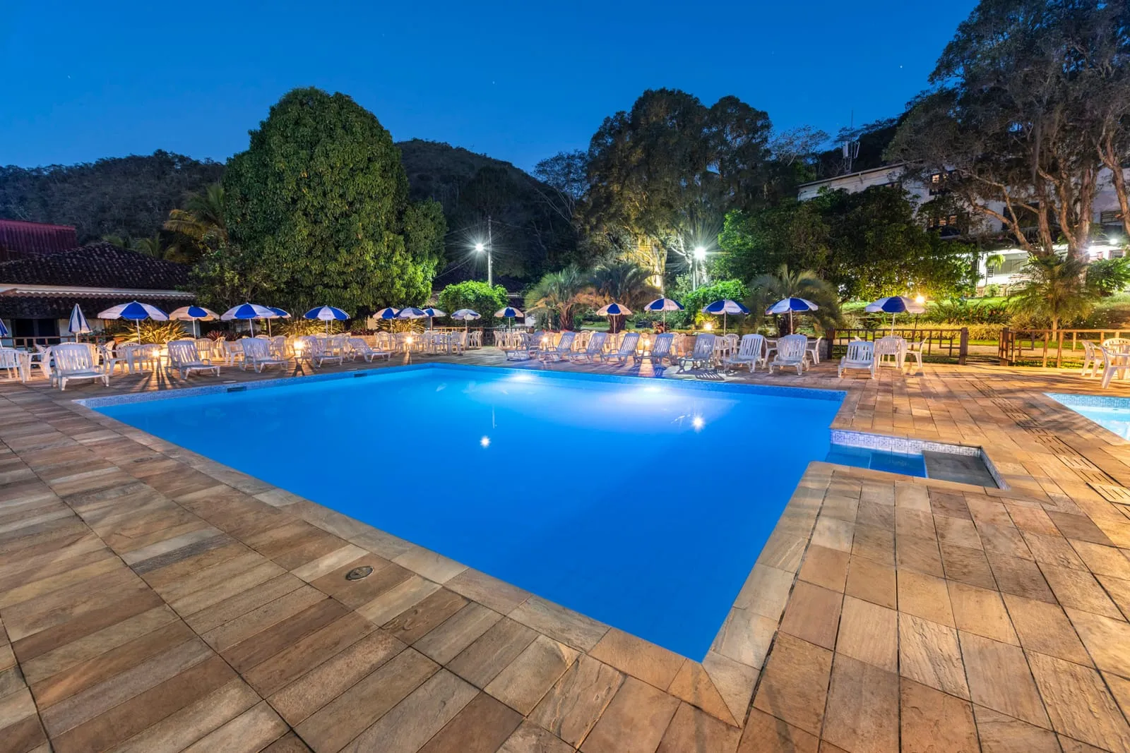 Piscina do Hotel Fazenda Cascatinha iluminada à noite, cercada de espreguiçadeiras