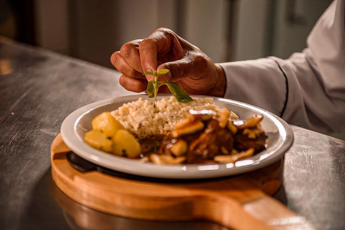 Chef finalizando prato com carne, arroz e batatas no restaurante do Minha Glória Hotel Boutique