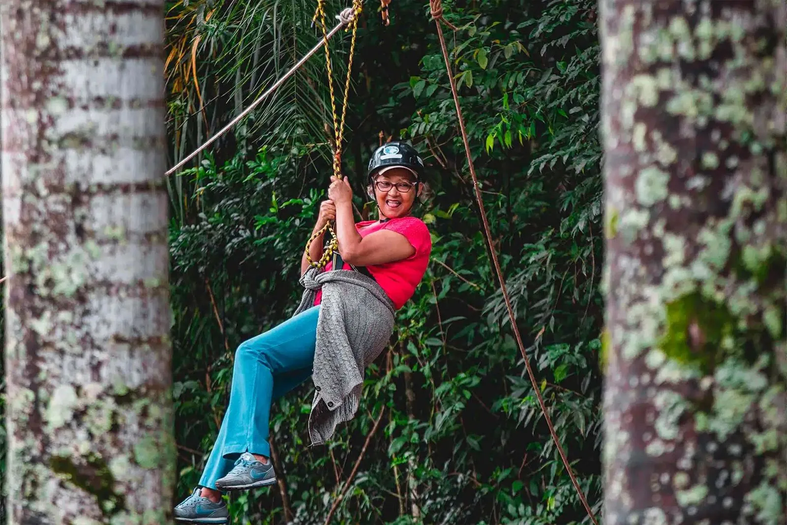 Hóspede sorrindo desce a tirolesa em meio à mata