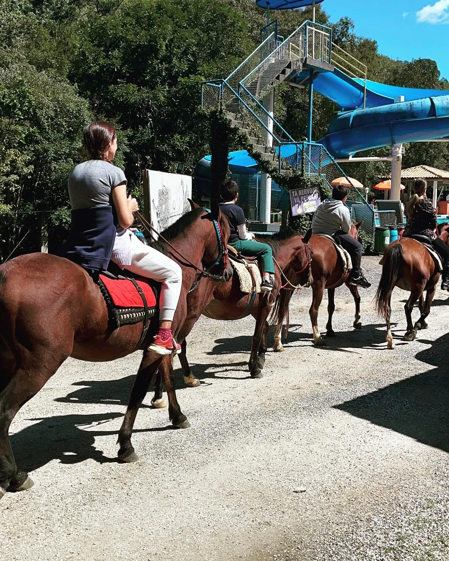 Cavalgada em fila com brinquedo aquático ao fundo na Pousada Fazenda Ribeirão das Flores