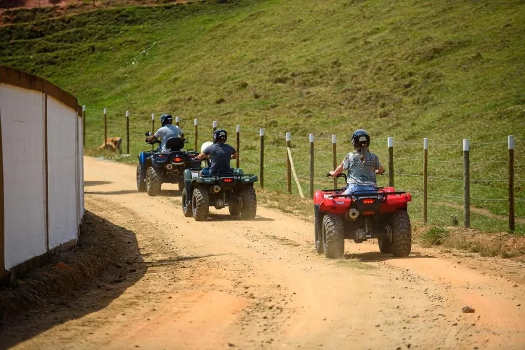 Hóspedes em passeio de quadriciclo por estrada de terra cercada de pasto