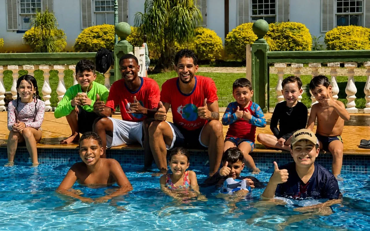 Crianças e monitores brincando na piscina do Hotel Fazenda Florença, com a capela ao fundo